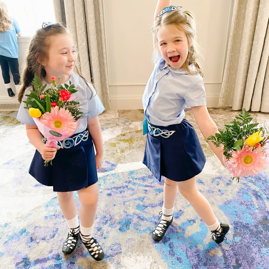 Two young Irish dancers doing a silly pose and holding flower bouquets. Irish dance class Halifax Bedford Dartmouth